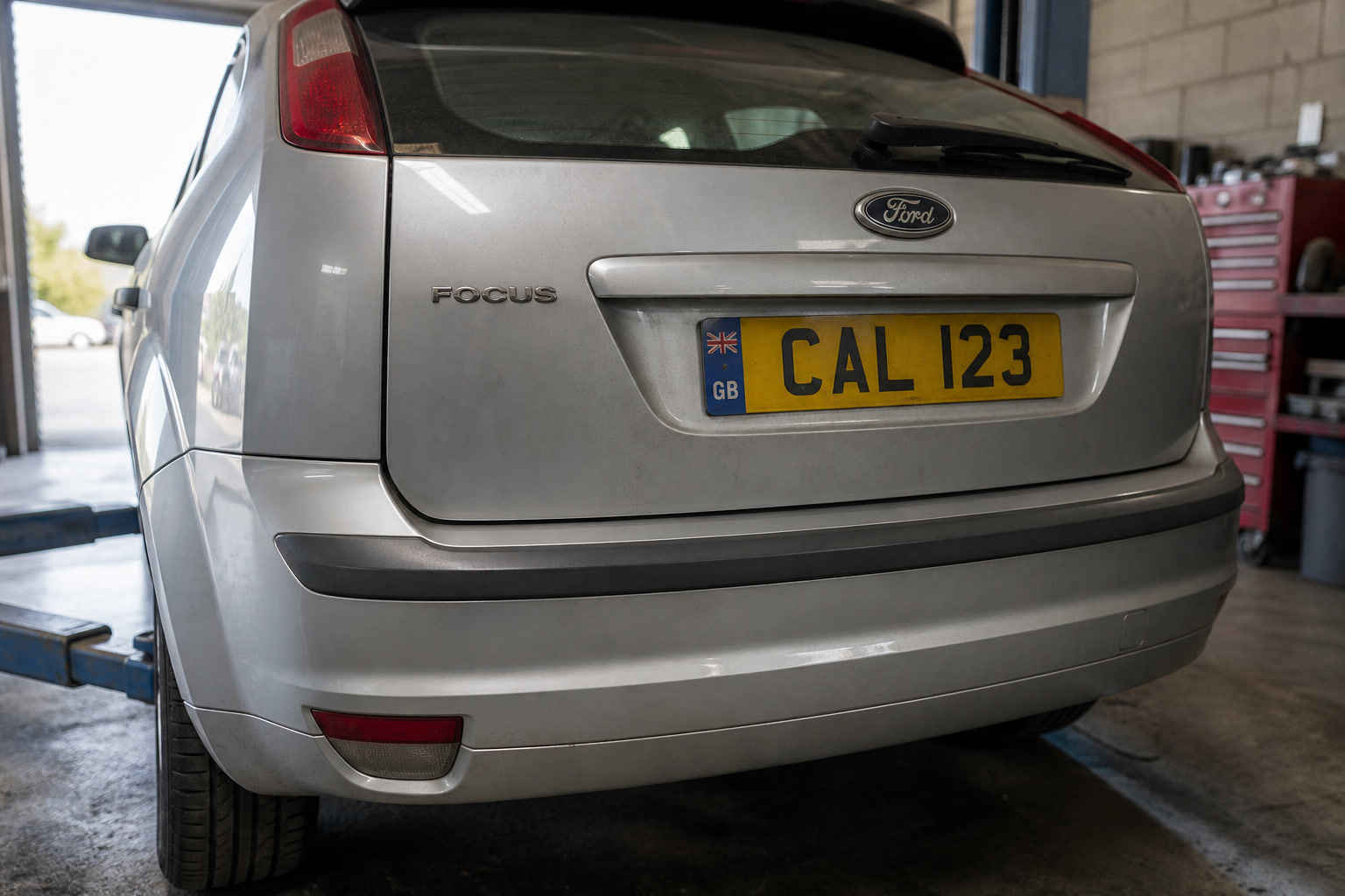 The rear of a Ford Focus on a ramp in a UK garage, yellow GB plate CAL 123.